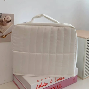 Close-up of white quilted cosmetic bag with top handle on a minimalist background