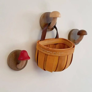 Three wooden mushroom wall hooks with one hanging a small basket on a cream wall