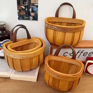 Three sizes of hand-woven wood storage baskets with leather handles in a rustic setting