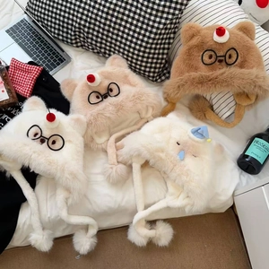 Détail de bonnets en peluche avec broderie de lunettes de chat et pompons présentés à plat
