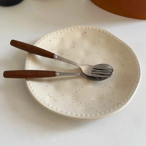 Detail of matte ink-splatter ceramic plate with irregular wavy edges and wooden cutlery