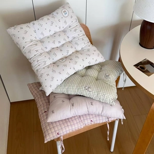 Detail of floral and checkered chair cushions with secure ties on a wooden chair
