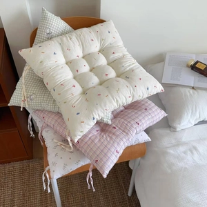 Floral and checkered thick soft chair cushions with ties stacked on a wooden chair