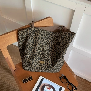 Leopard print canvas tote bag detail featuring golden handmade metal logo and brown lining