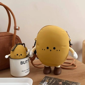 Detail of cute yellow potato silicone crossbody bag with mini charm on a wooden desk