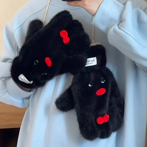 Dettaglio di guanti in peluche nera con design a pinguino e fiocco rosso decorativo
