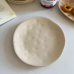 Detail of cream ceramic plate with black ink splashes and pearl relief edges
