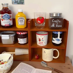 Three-tier wooden storage shelf showcasing kitchen spice jars and mugs in a home setting