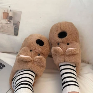 Detalle de pantuflas de oso pardo de peluche con orejas 3D en una cama blanca