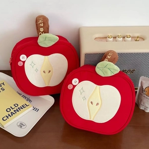 Detailed view of red plush apple-shaped cosmetic bags with embroidery on a wooden table