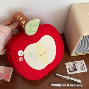 Detail of red apple-shaped makeup bag featuring embroidered core and fabric texture