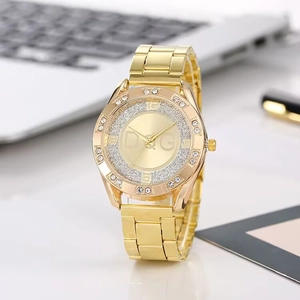 Elegant gold metal watch with rhinestones and glitter dial on a modern desk setup