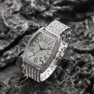 Macro detail of silver tonneau-shaped watch featuring iced-out crystals and bold numerals