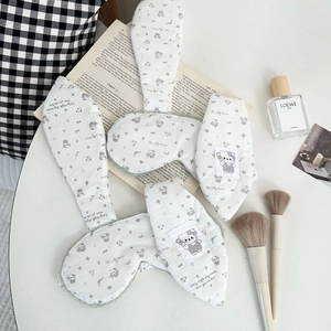 Detail of white cotton sleep mask with bunny ears and lace trim on a book background