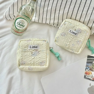 Detail of two cream quilted cotton pouches with mint green zipper pulls on a bed