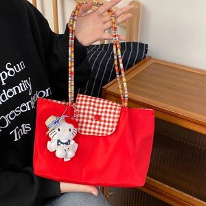 Close-up of red canvas tote bag with woven colorful handle and plaid flap detail