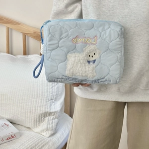 Detail of light blue quilted cosmetic bag with cute lamb embroidery and hand strap