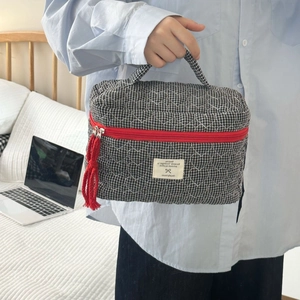 Détail de la trousse matelassée avec fermeture éclair rouge et pompon décoratif