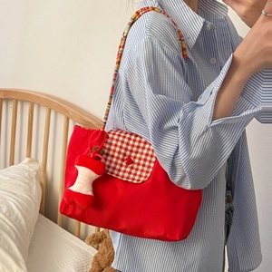 Detail of red tote bag with plaid flap, colorful beaded strap and apple plush charm decor