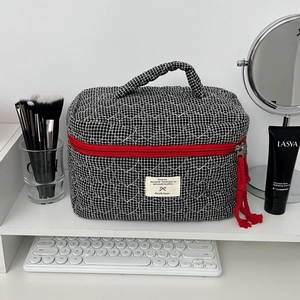 Détail d'une trousse à maquillage matelassée en damier noir et blanc avec gland rouge