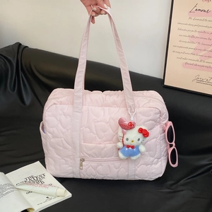 Sac de voyage rose matelassé cœur avec double anse et poche latérale sur canapé