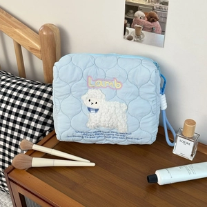 Detail of blue quilted cosmetic bag with white lamb patch on a wooden nightstand
