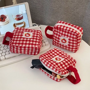 Detailed view of red plaid plush cosmetic bags holding sunglasses and lipstick on desk