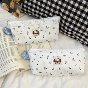 Close-up of floral cat pencil pouch with white lace trim and blue heart charm on book
