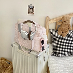 Sac de voyage matelassé rose avec passant pour valise posé sur un bagage blanc
