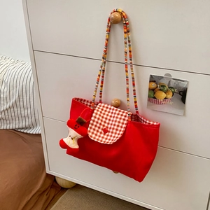 Detail of red checkered canvas tote bag with woven strap and plush apple charm accessory