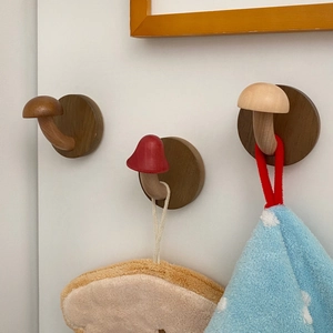Three mushroom shaped wooden wall hooks in various colors mounted on a white wall
