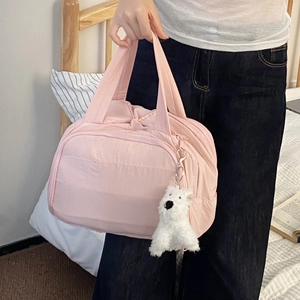 Pink quilted travel organizer bag with plush puppy pendant shown in a cozy bedroom setting