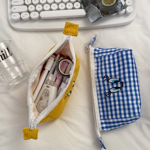 Detail of yellow corduroy and blue plaid pouches filled with stationery on a desk