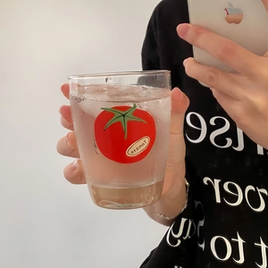 Close-up of a clear tomato print glass cup with ice cubes held by a person