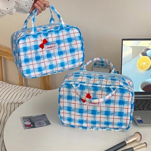 Detail of blue plaid makeup bag featuring red bow decoration and sturdy double handles
