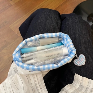Detail of white floral pencil case with blue checkered interior and heart-shaped charm