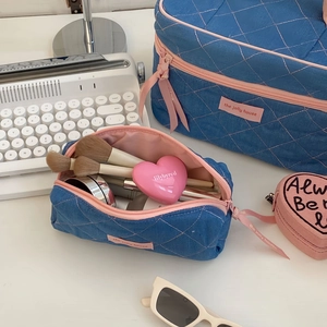 Close-up of quilted denim makeup bags with pink stitching on a styled white desktop