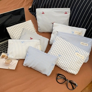 Flat lay of bow-embroidered striped canvas cosmetic bags with laptop and travel accessories