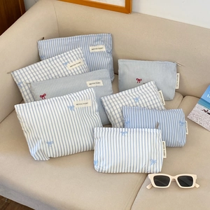 Close-up of blue and white striped fabric makeup bags with bow embroidery on a beige sofa