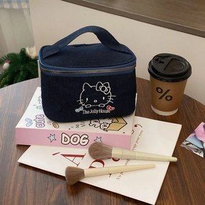 Detail of blue denim cat cosmetic bag with white embroidery on a wooden table setup