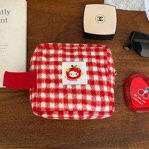 Detail of a red checkered makeup bag with side handle on a dark wooden table background