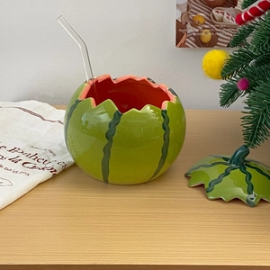 Detail of creative ceramic watermelon bowl with lid and glass straw on a wooden table