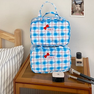 Detailed view of checkered blue and red makeup bags with cute bow embroidery on wood
