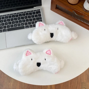 Close-up of soft white plush Westie dog sleep mask on a cozy desk setting