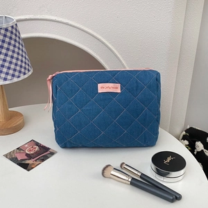 Close-up of blue quilted denim toiletry bag with pink zipper and logo label