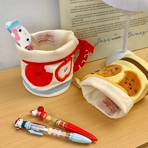 Detail of canvas cup-shaped pencil cases with embroidered apple and cookie patterns