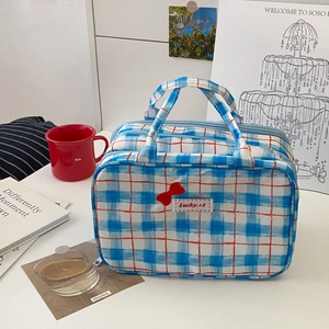 Close-up of blue plaid makeup bag with red bow accent and Lucky embroidery detail