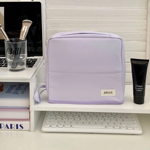 Lavender fabric toiletry bag with JOLLY tag shown in a clean desktop storage scene