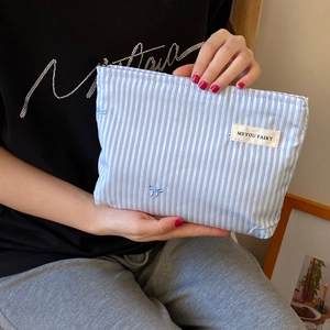 Detail of hand-held blue striped cosmetic bag with bow embroidery and zipper closure