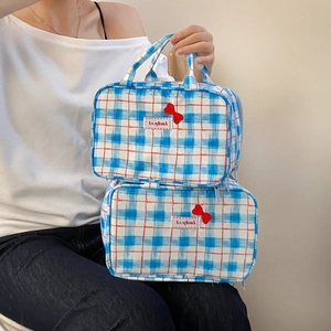 Blue plaid makeup bag with red bow detail and top handle shown in a hand-held view